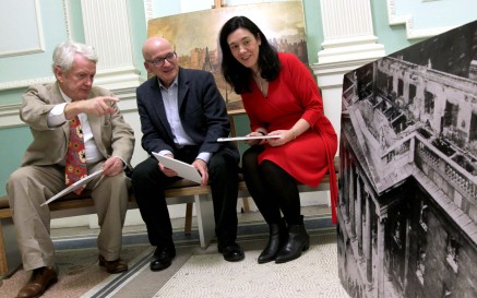 Three people sit and observe a large-scale black and white photograph