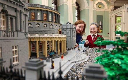 An Stiúrthóir Gníomhach Katherine McSharry agus leanbh ina seasamh in aice le tosach múnla Lego de chuid NLI